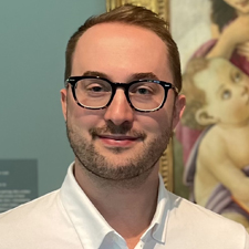 portrait of a man with glasses in front of a Renaissance painting